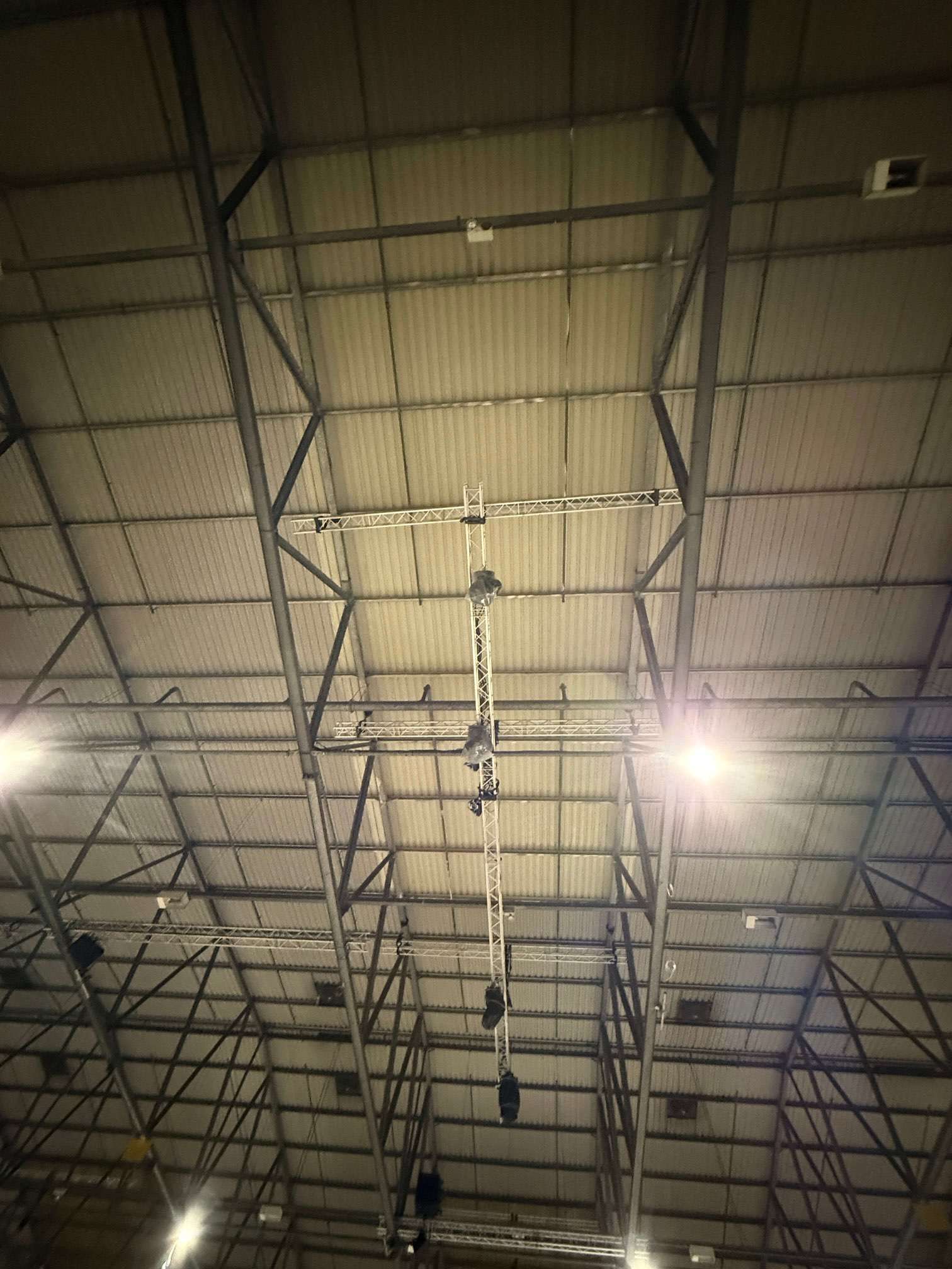Suspended lighting rig beneath warehouse roof panels and steel trusses