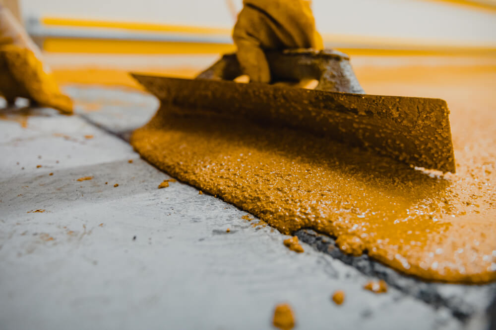 Close-up of an orange floor coating being levelled with a hand trowel.