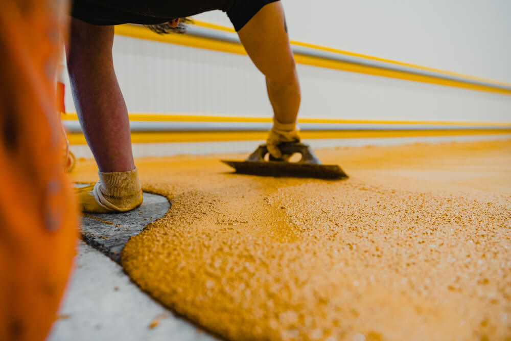 Worker smoothing an orange floor coating with a hand trowel.