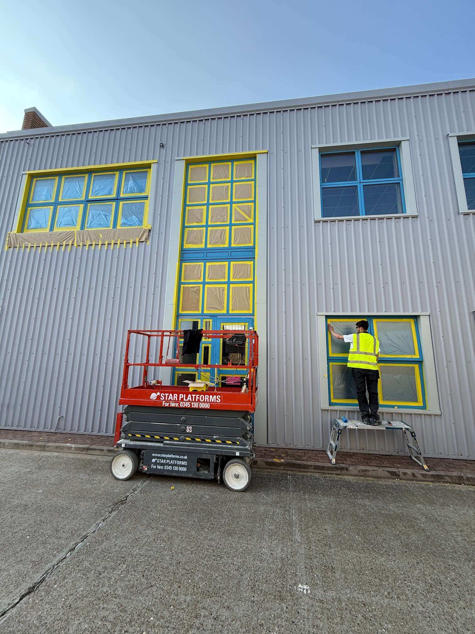 Workers preparing masked window frames beside a raised access platform.