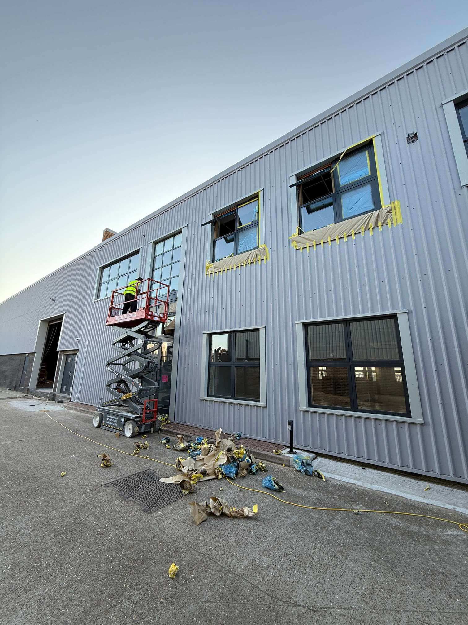 Scissor lift positioned beneath masked upper-storey windows on a metal-clad building.