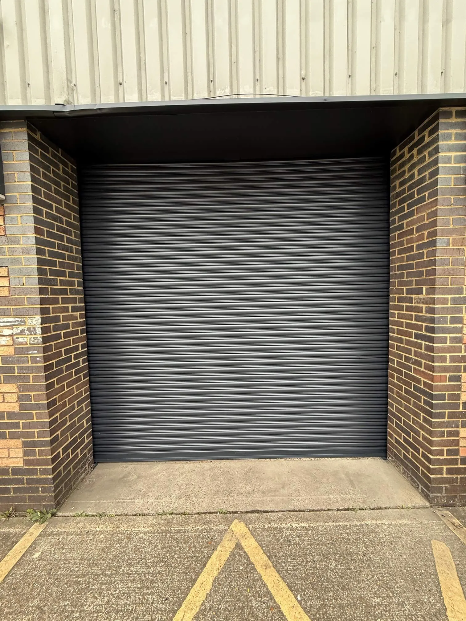 Dark grey roller shutter between brick piers at an industrial unit.