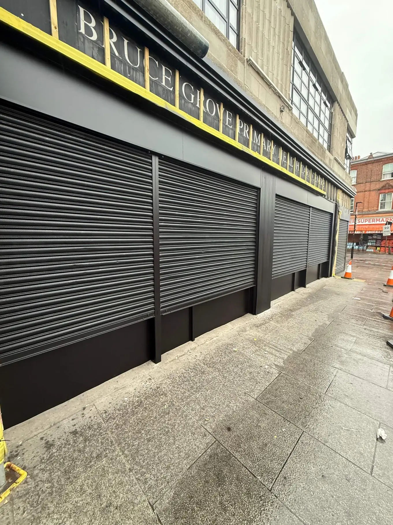 Dark-coated roller shutters across the frontage of Bruce Grove Primary Health Care Centre.