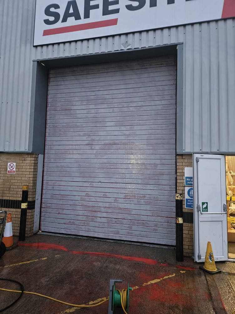 Grey industrial roller shutter beneath a Safesite sign, with preparation equipment outside.