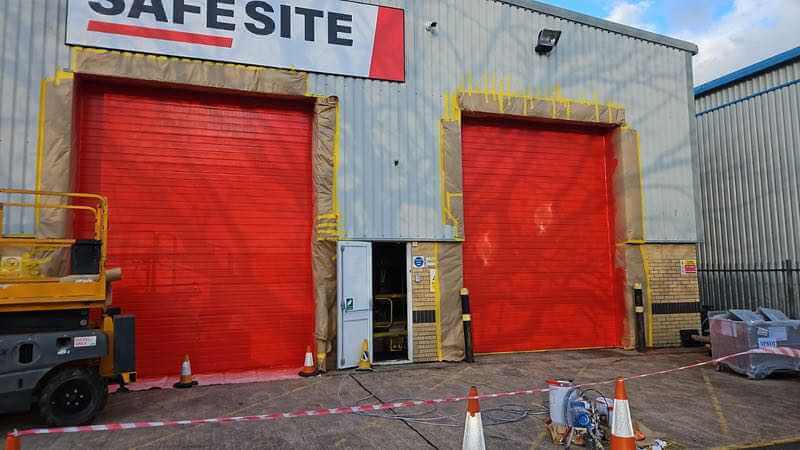 Two red-coated industrial roller shutters with protective masking around their openings.