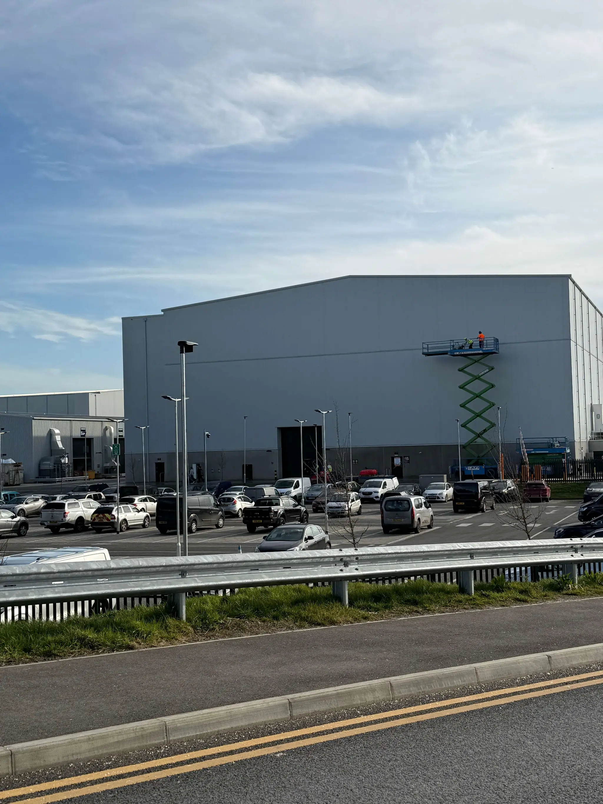Light-coloured studio facade with a raised scissor lift and vehicles outside