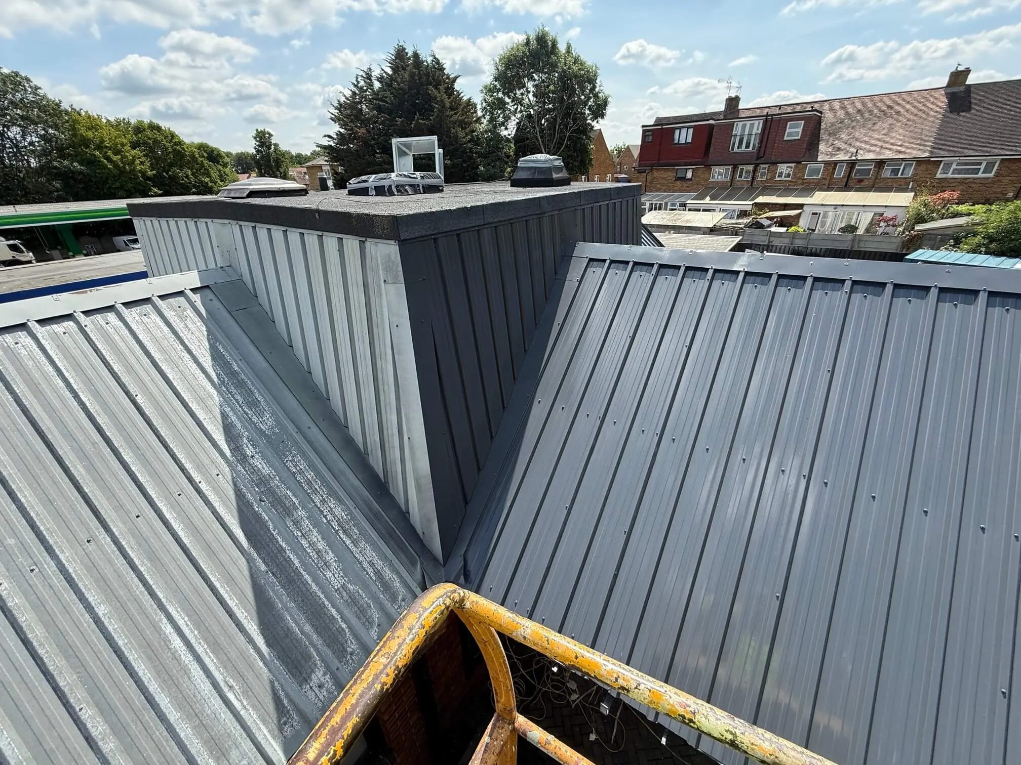 Partially prepared metal roof slopes beside a central plant enclosure.