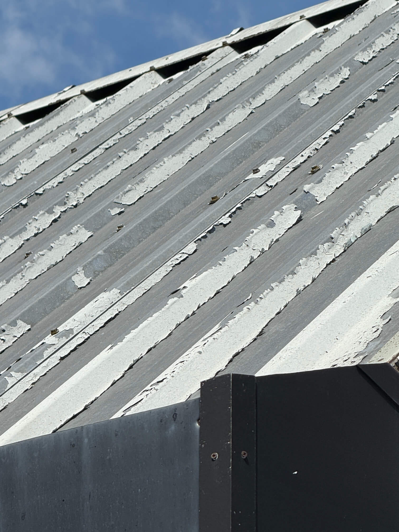 Peeling coating on profiled metal roof sheets before refurbishment.
