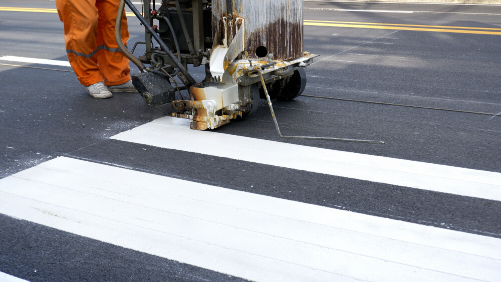 Operator using road-marking equipment to apply white crossing stripes.