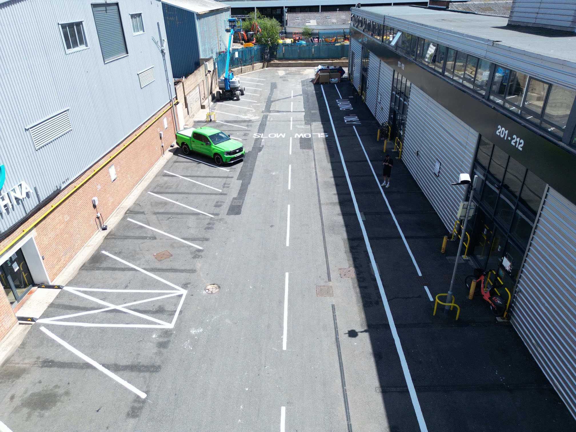 Fresh white parking-bay lines, centre markings and slow lettering on an industrial road.