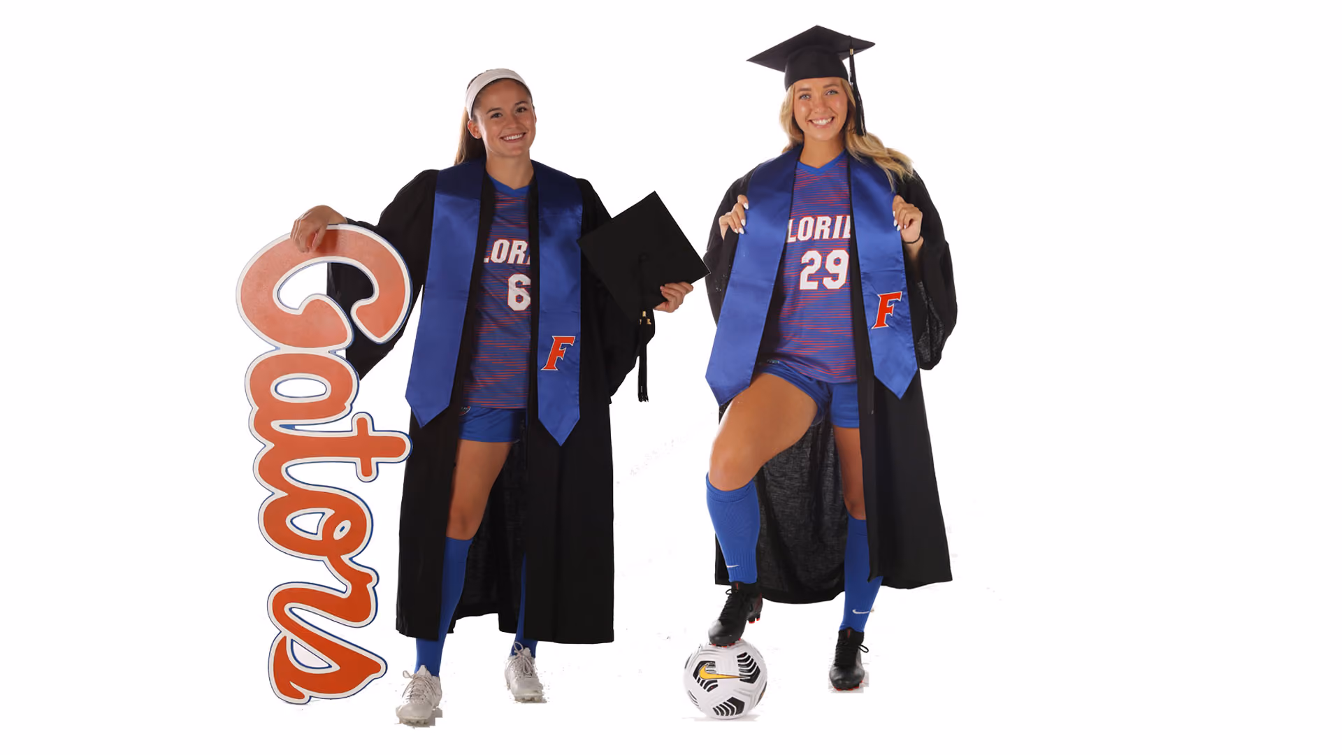 Two female soccer players in graduation gowns and caps, one holding a 'Gators' sign, the other with foot on soccer ball.