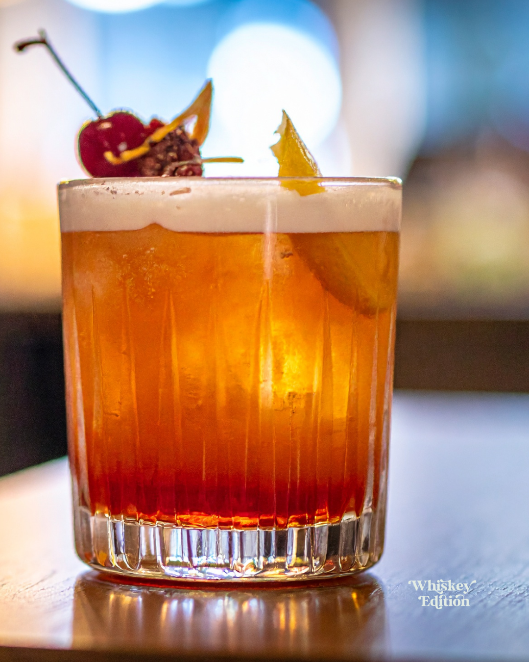 Whiskey Sour in a rocks glass with ice, garnished with a cocktail cherry