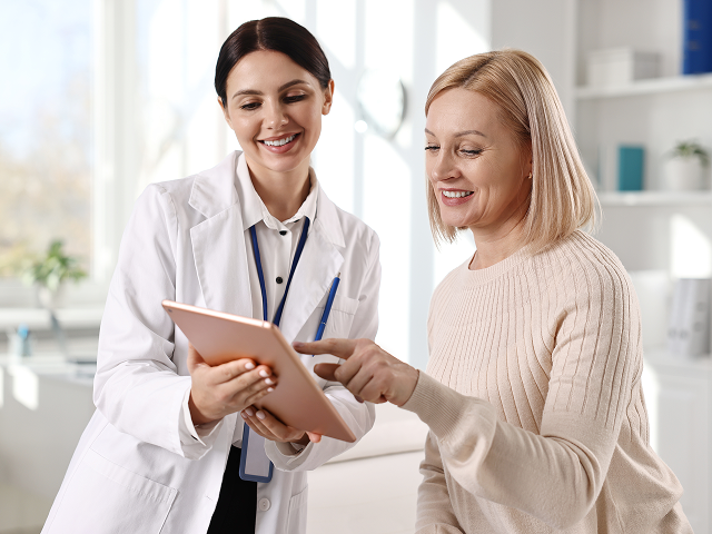 Female doctor showing a tablet to a smiling woman in a bright medical office.