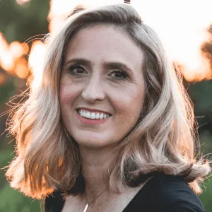 Smiling woman with shoulder-length blonde hair outdoors during golden hour light.