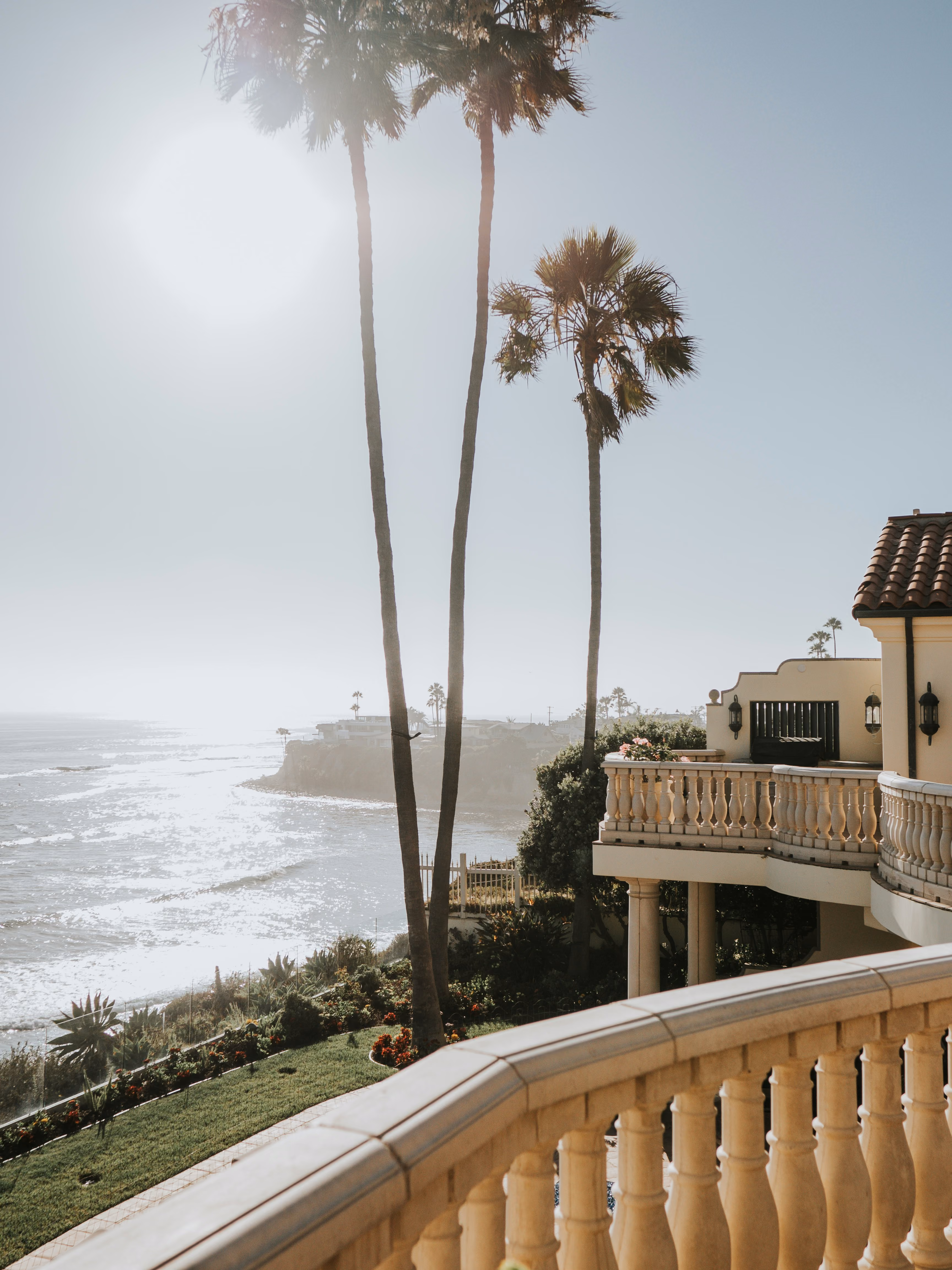 Ocean view with tall palm trees and a balcony from a Mediterranean-style house.