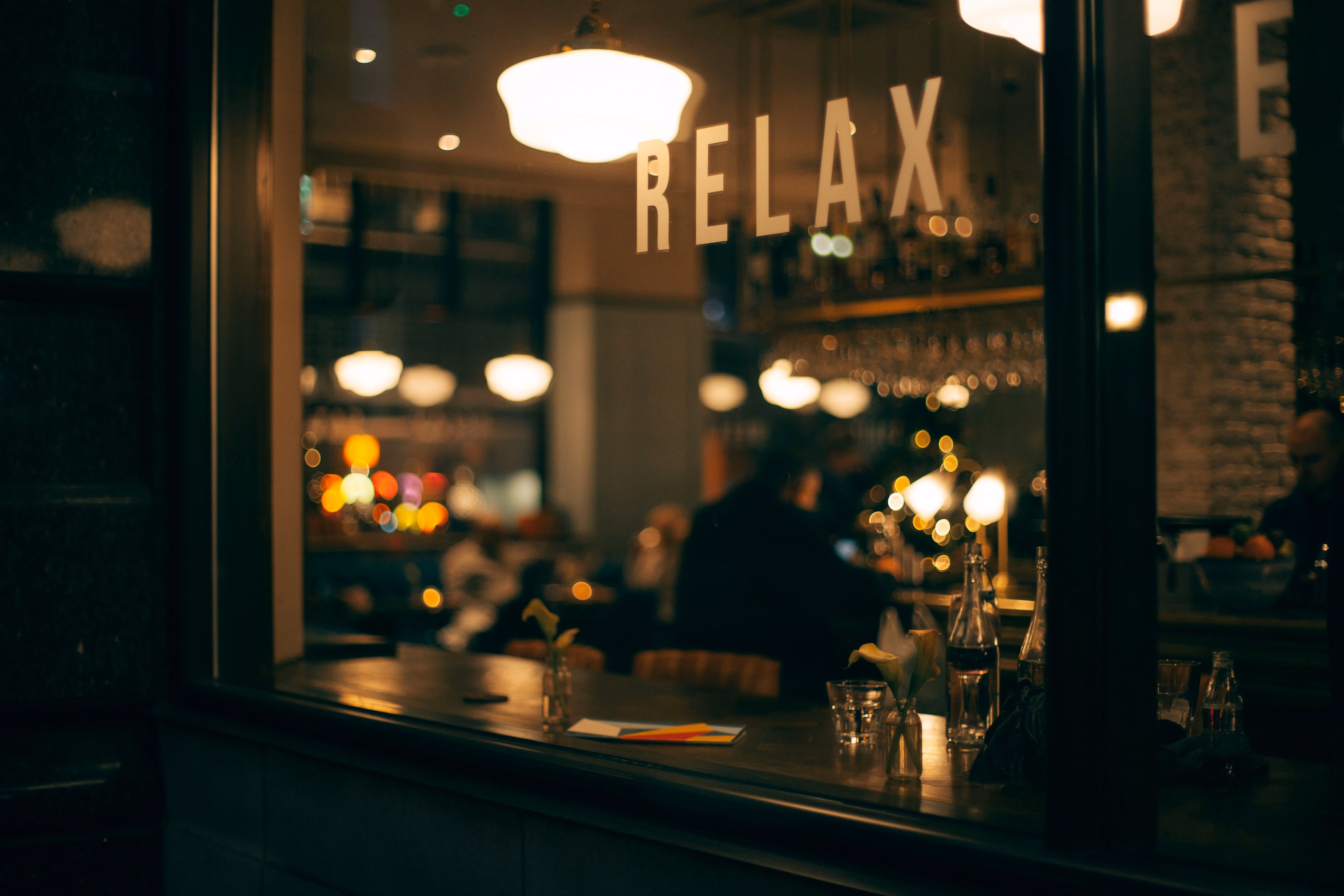 View into a warmly lit bar with people and a window decal saying RELAX.