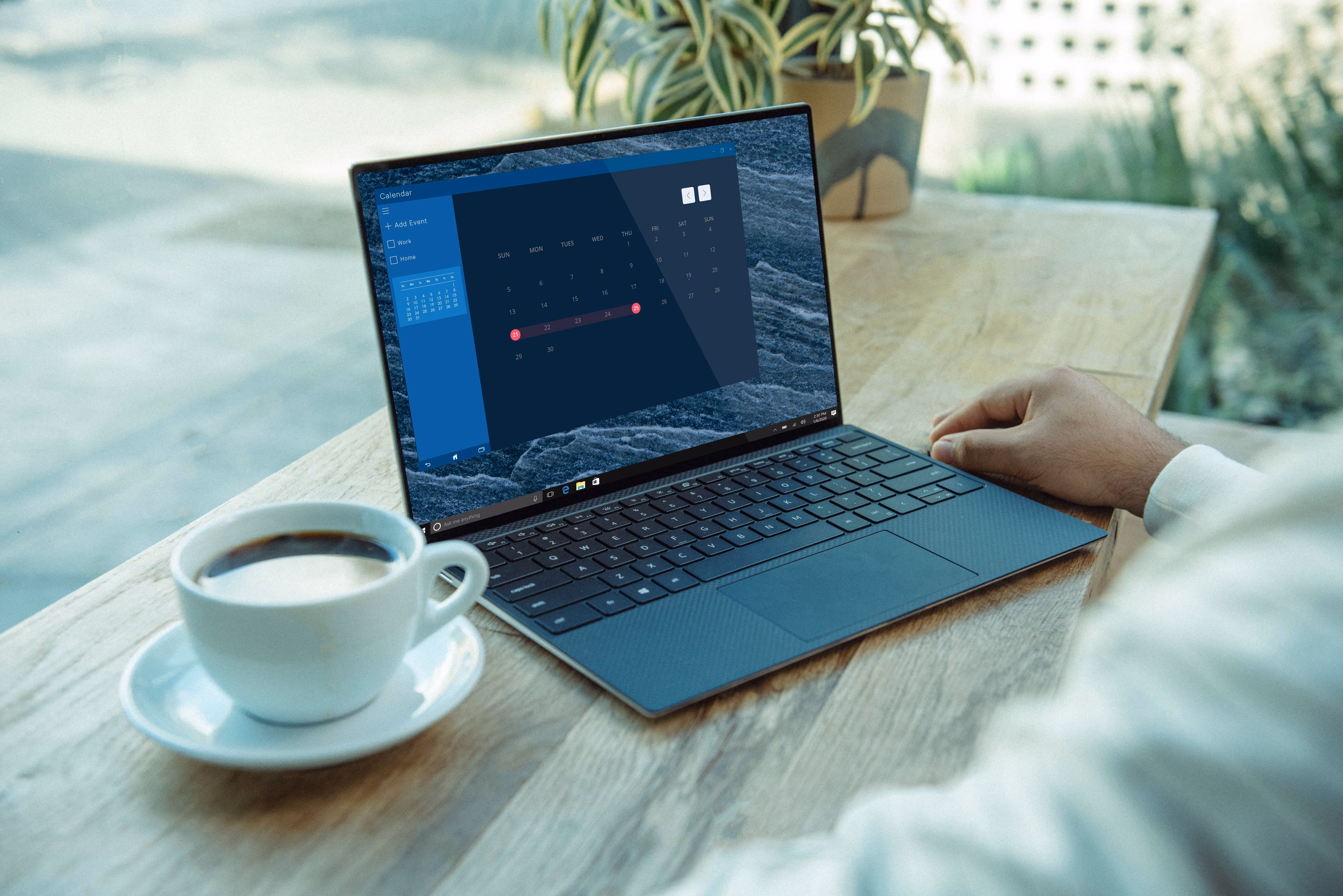 Person using a laptop with calendar app open at a table with a cup of coffee and plant in background.