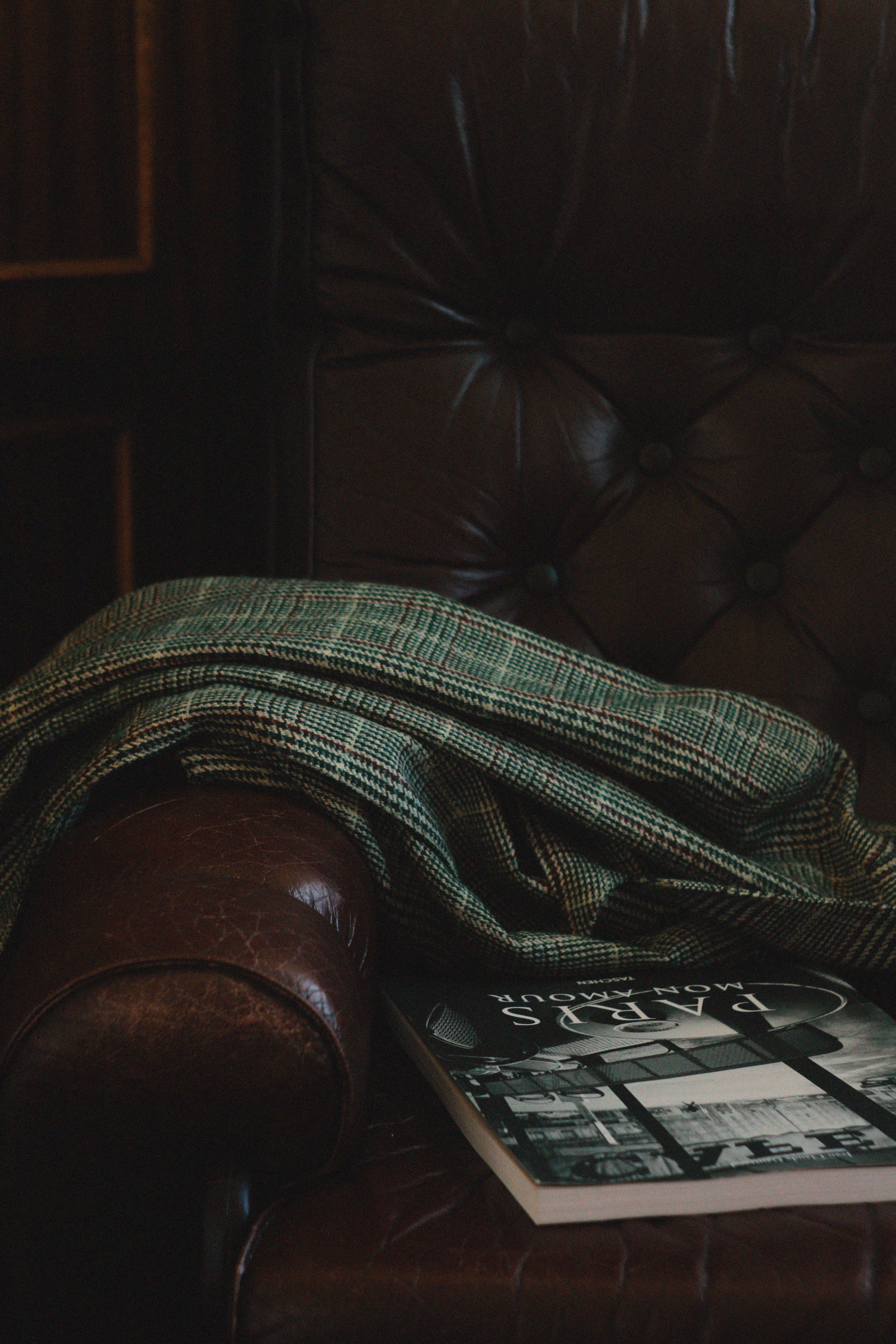 Green plaid fabric draped over a brown leather tufted armchair with a book titled Paris Mon Amour.