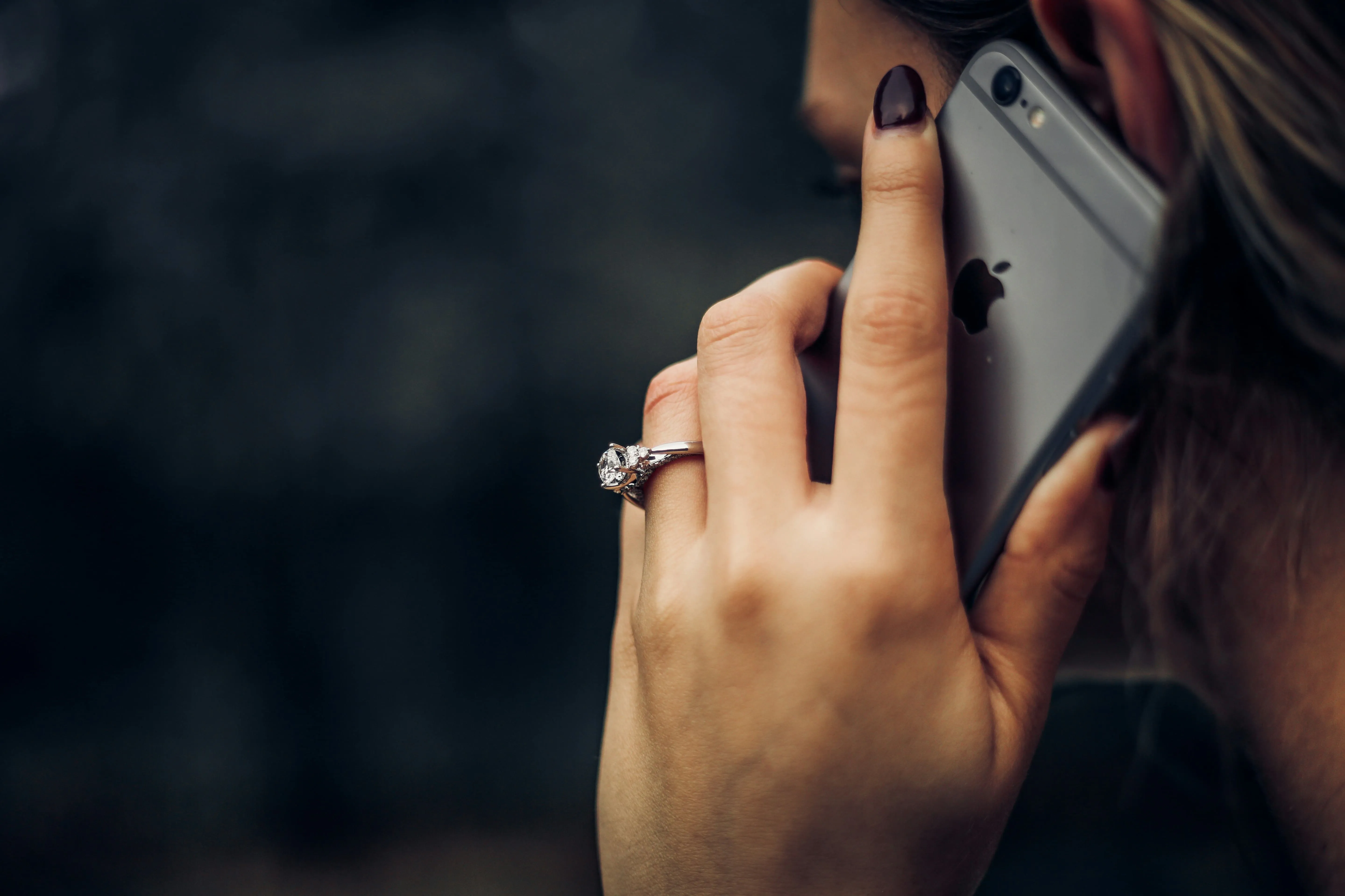 Close-up of a woman's hand with a diamond ring holding an iPhone to her ear.