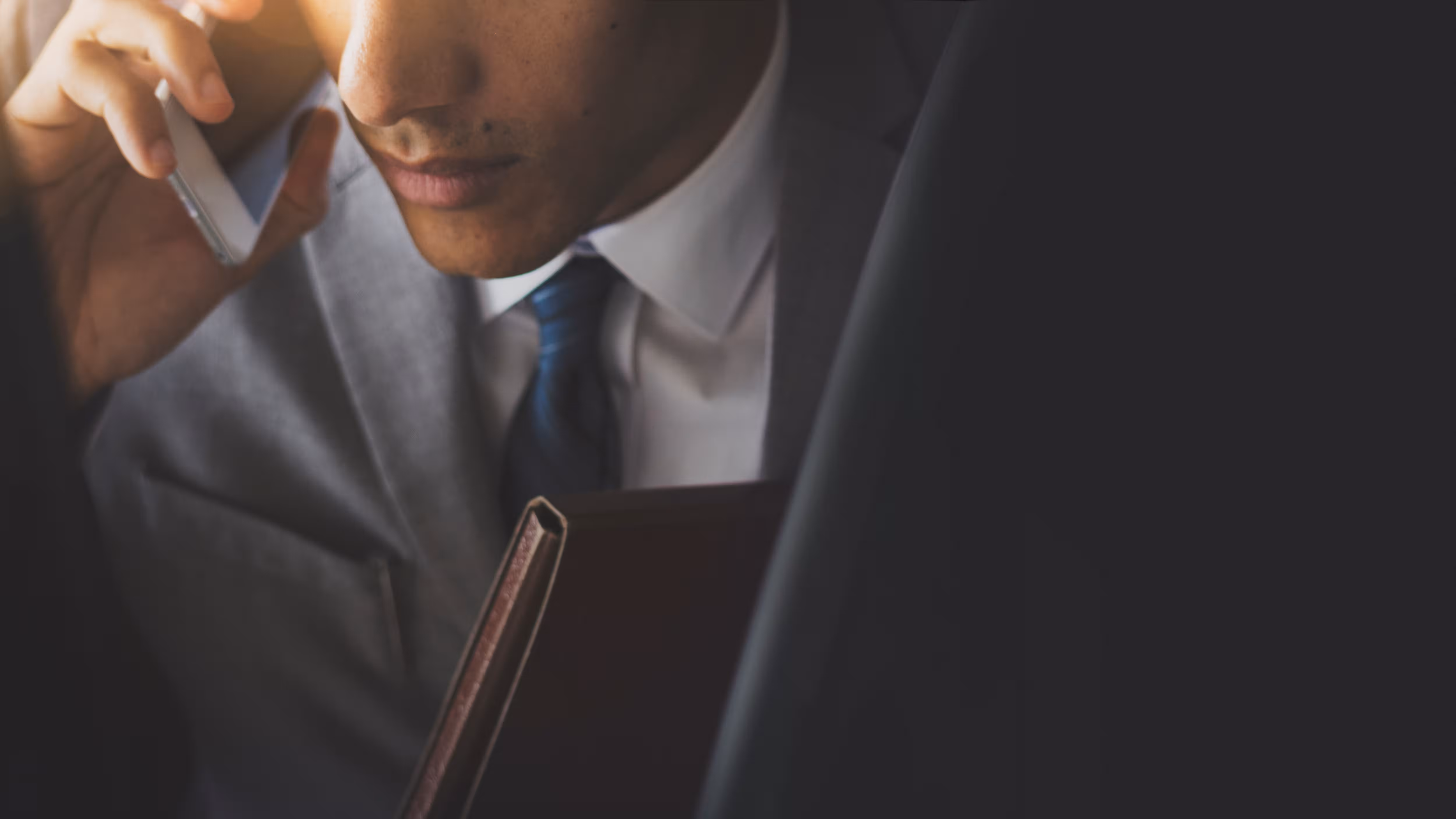 Businessman in a gray suit talking on the phone and holding a leather folder.
