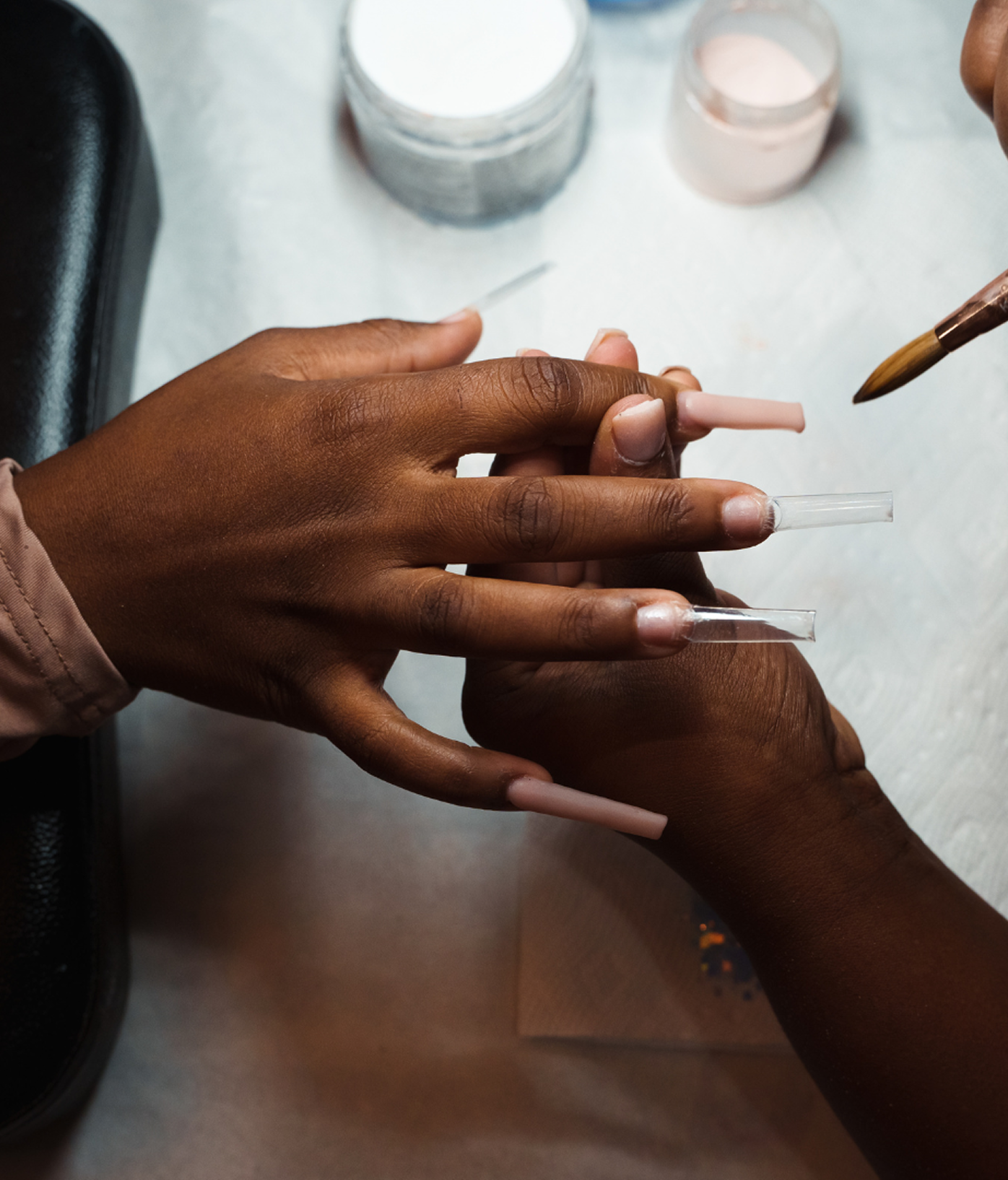 A technician fitting clear nail extensions to a guest's hand