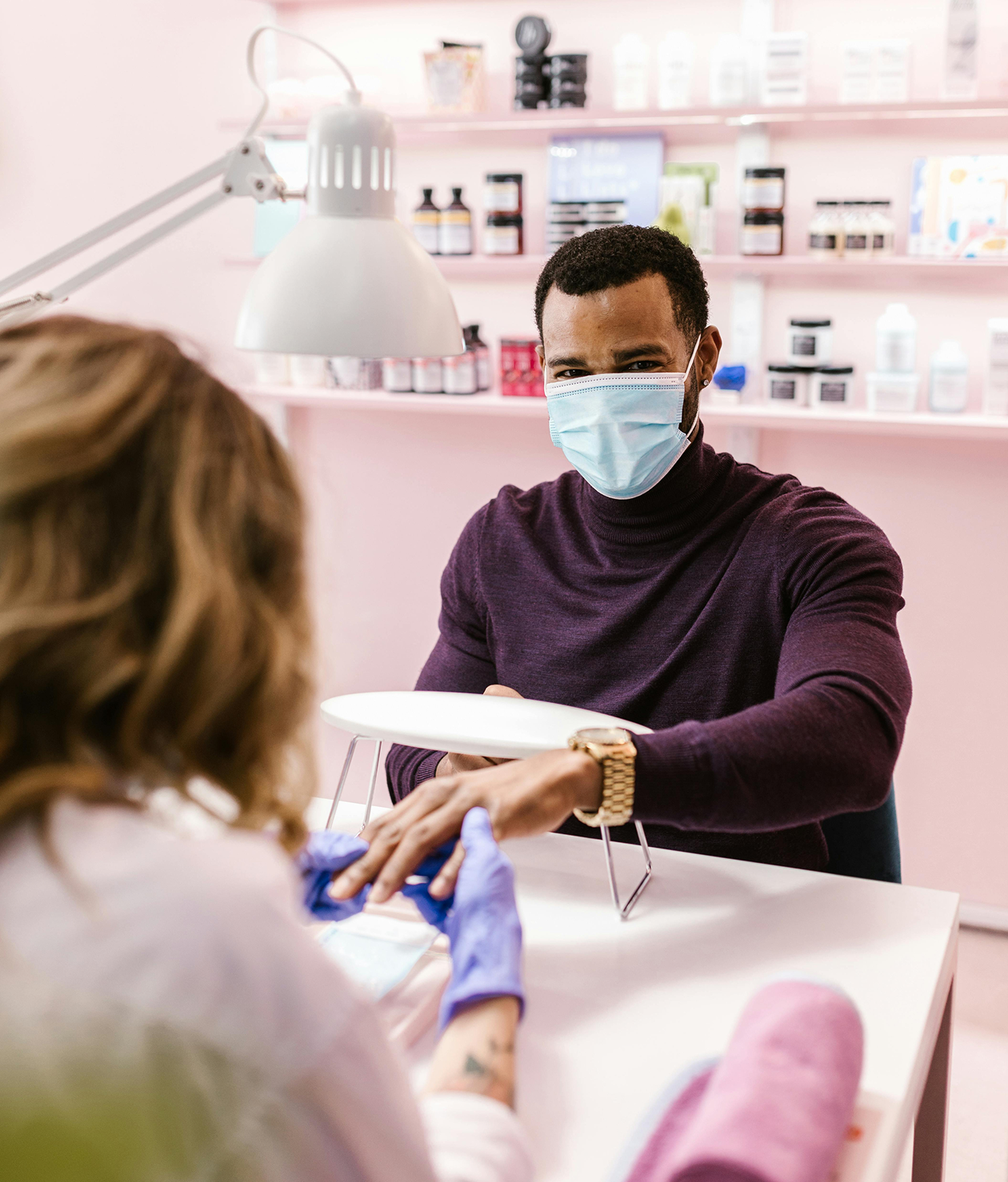 A masked nail technician working with a guest at a service station