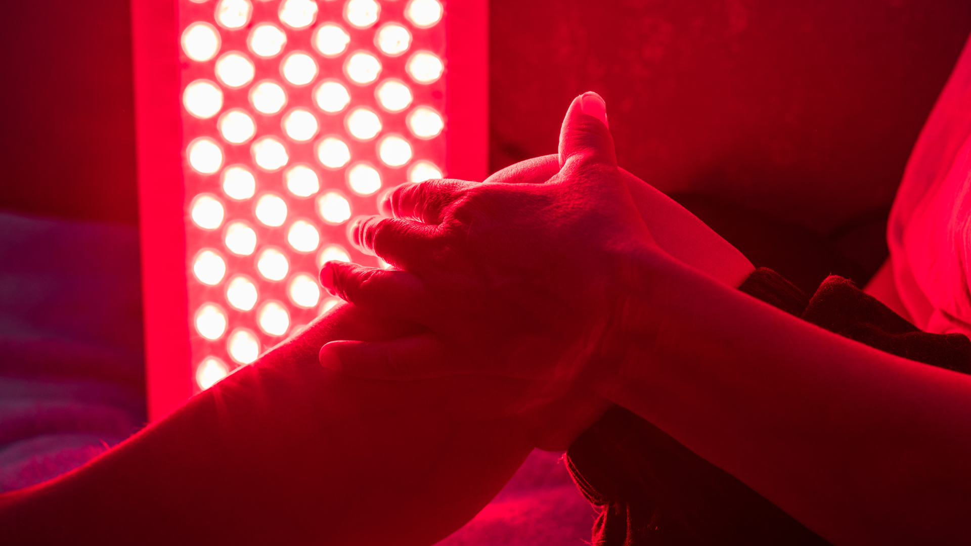Hands resting beneath a red light therapy panel