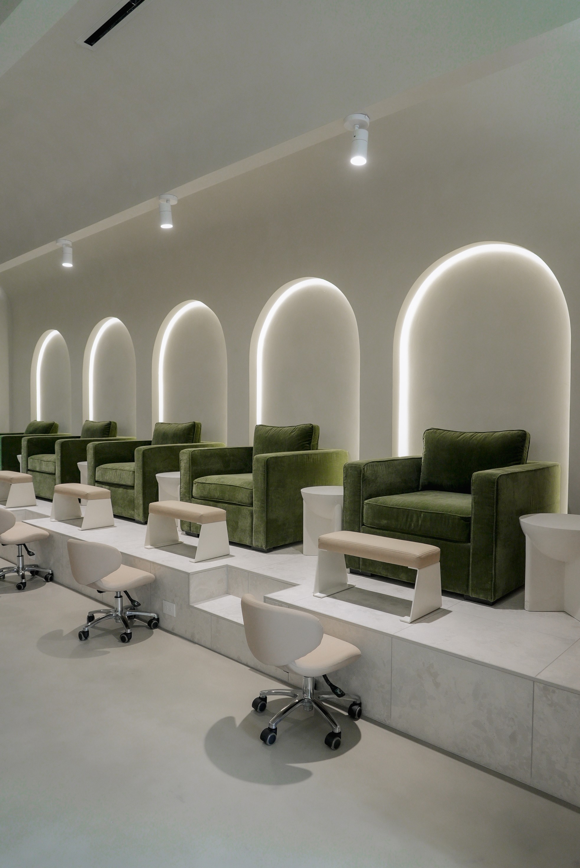Green velvet pedicure chairs beneath the studio's backlit arches