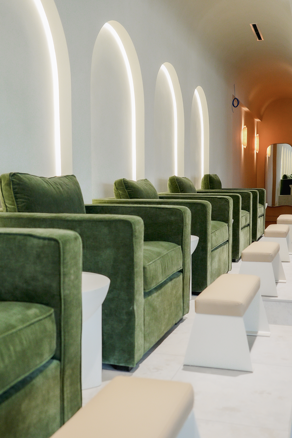 Green velvet pedicure chairs beneath backlit arches