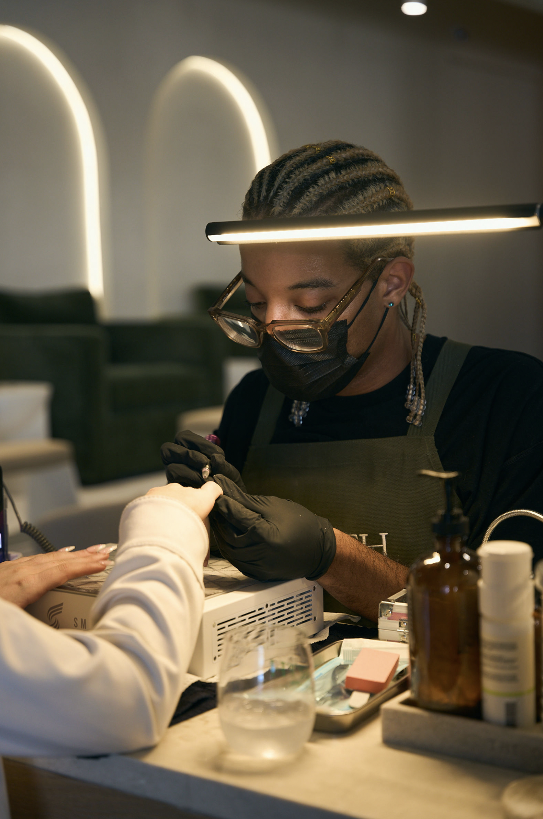 A masked technician working at a nail station
