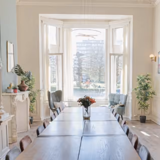 Bright conference room with wooden table, chairs, large window, plants, and decorative fireplace.