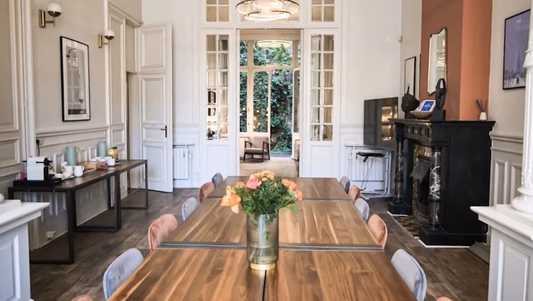 Elegant conference room with wooden table, chairs, flowers, fireplace, and open French doors to garden.