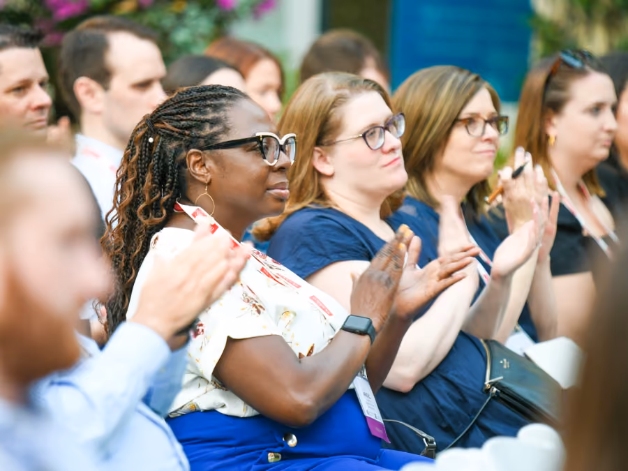 Audience of diverse adults seated and clapping during an event or presentation.