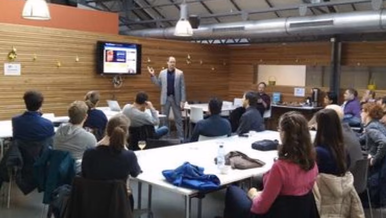 Man in gray suit giving a presentation to seated audience in a modern conference room.