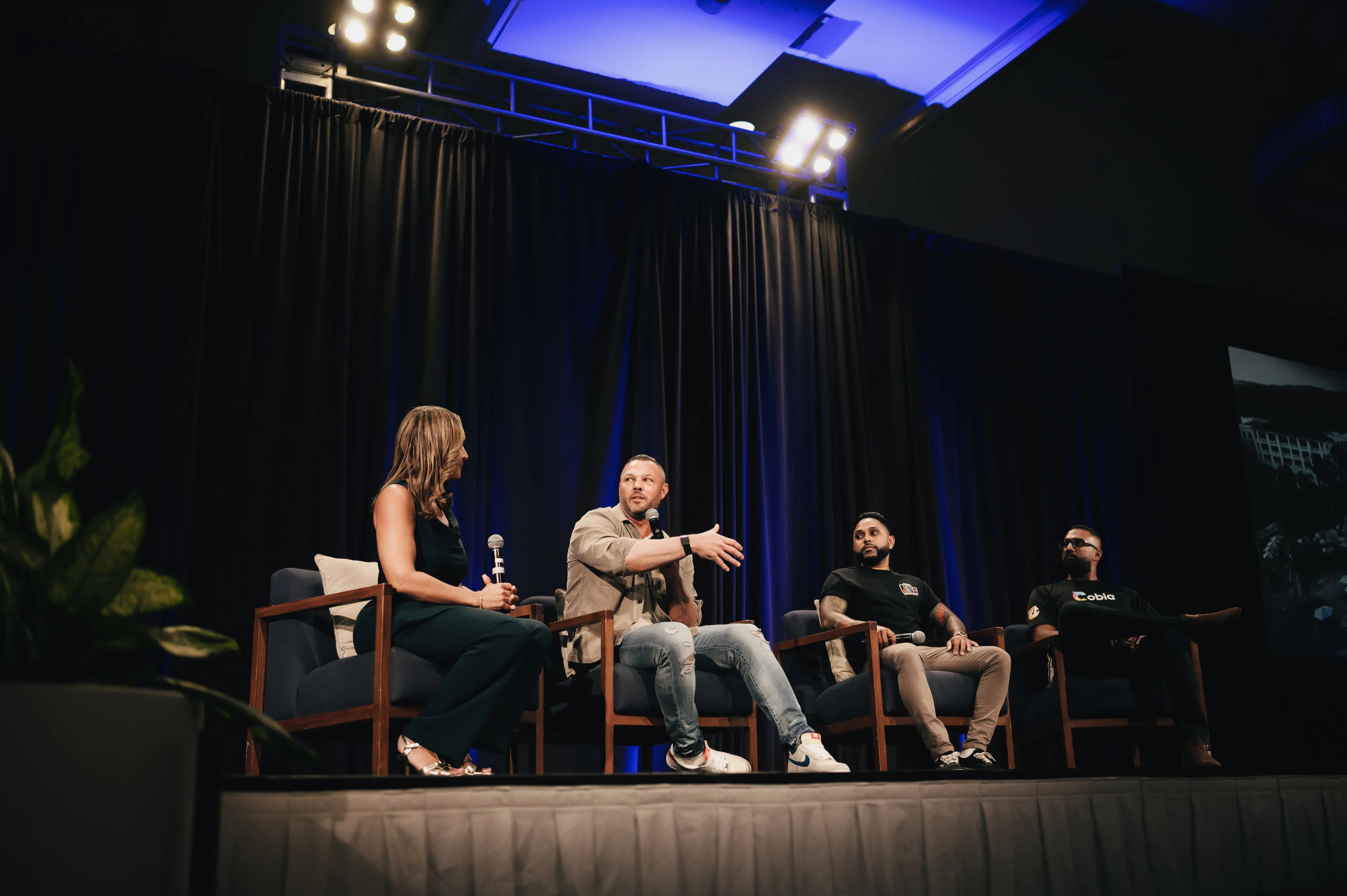 Four people seated on stage chairs in a panel discussion under bright lights and dark curtains.