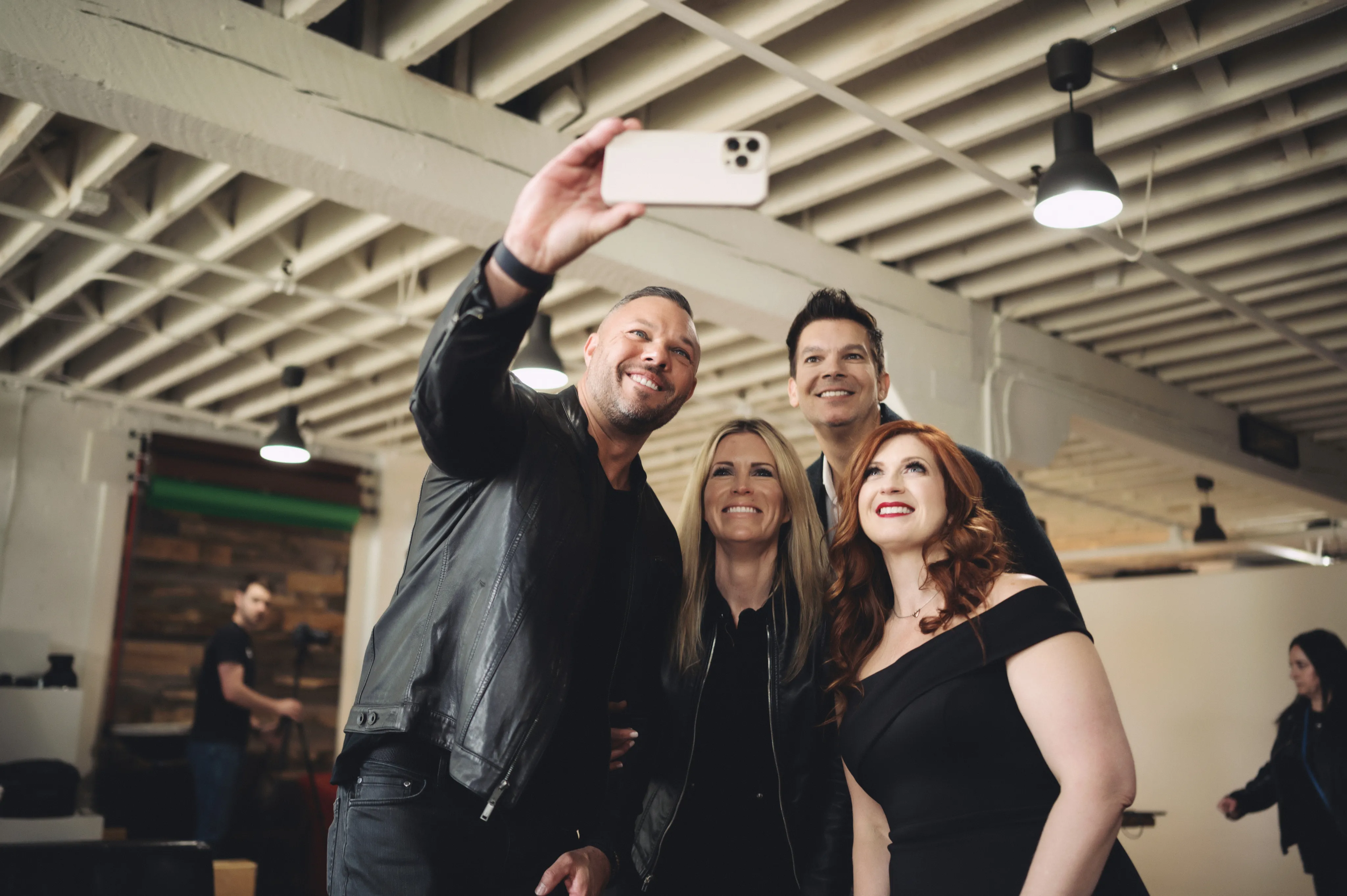 Four adults smiling and posing for a selfie in a spacious, industrial-style room.
