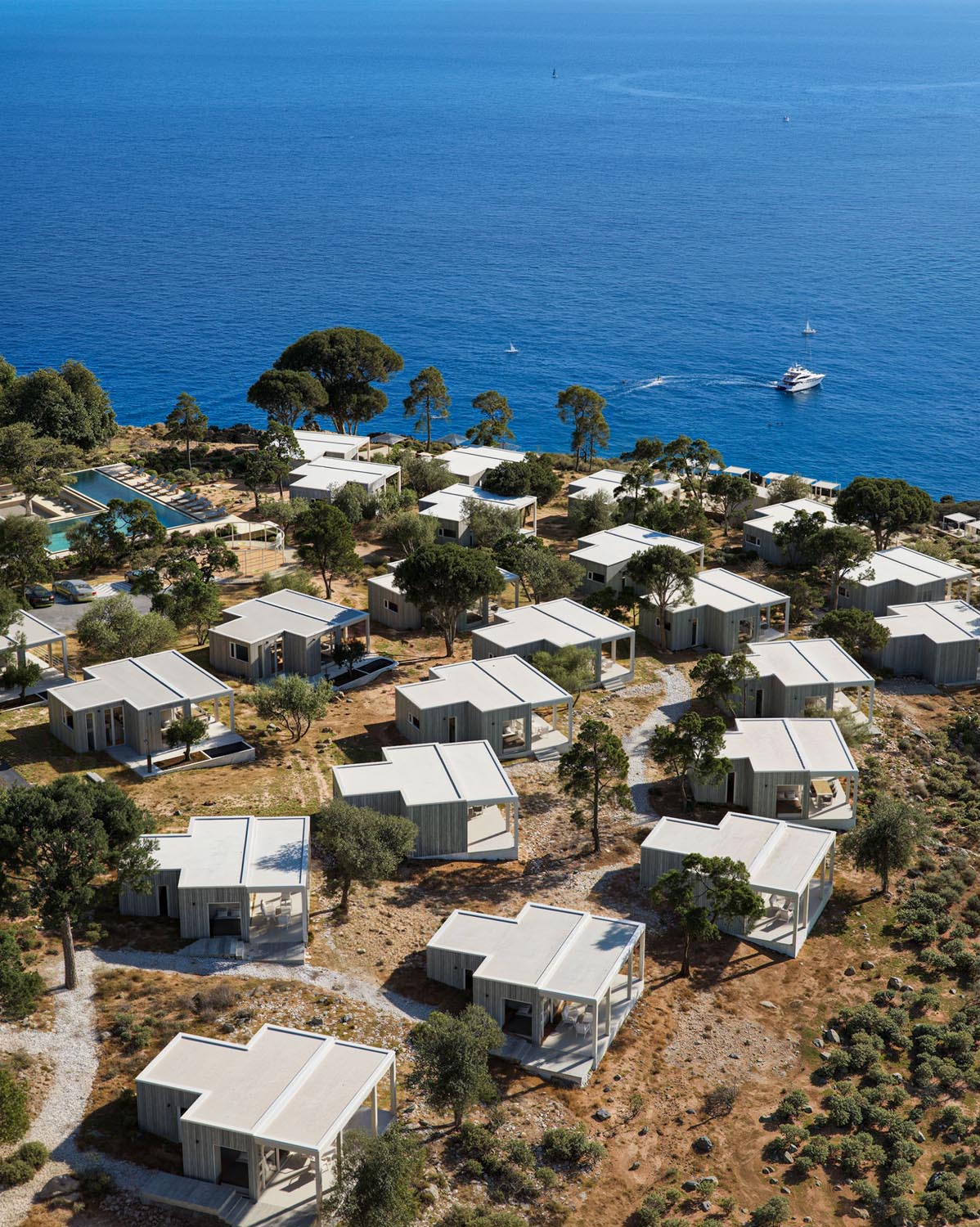Beachfront resort with multiple white modern cottages on dry land near blue ocean water and boats.
