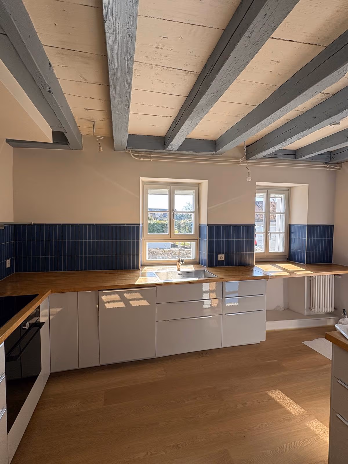 Cuisine rénovée avec crédence carrelée bleue, plan de travail en bois et meubles blancs