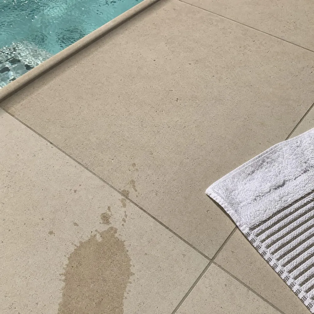 Margelle de piscine en travertin beige clair avec serviette posée au sol