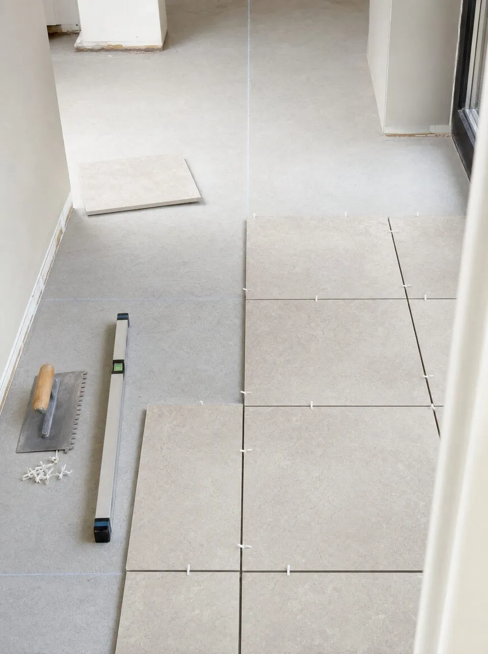 Carreaux grand format disposés au sol avec croisillons, niveau et truelle crantée avant la pose