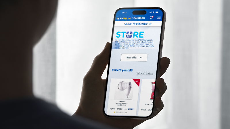 Persona che tiene un telefono con l'app PAYBACK aperta, mostra punti e prodotti in offerta.