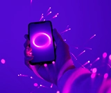 Mano che tiene smartphone acceso con sfondo vibrante viola e scintille luminose.