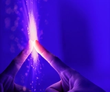 Due dita che si toccano con scintille di luce viola tra di loro su sfondo blu.