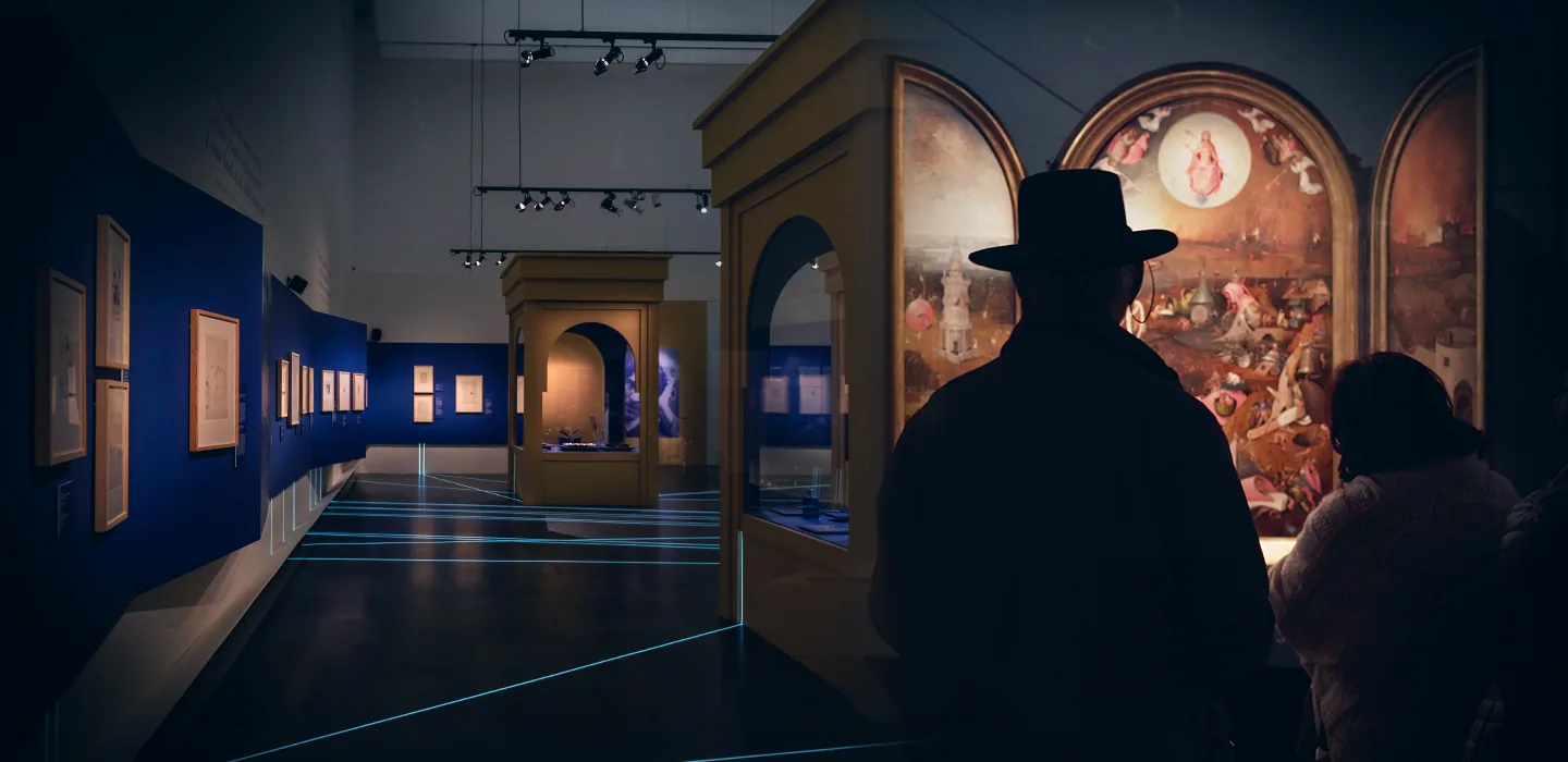 Persone che osservano dipinti antichi in una galleria d'arte con luci e pareti blu.