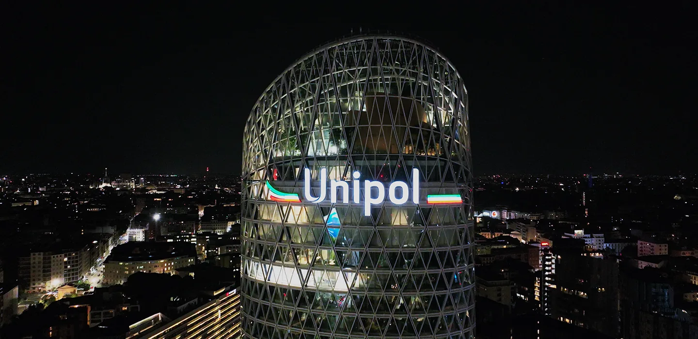 Grattacielo Unipol illuminato di notte in una città con skyline urbano sullo sfondo.