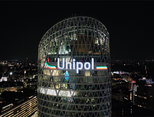 Grattacielo Unipol di notte con logo illuminato e vista di città sullo sfondo.