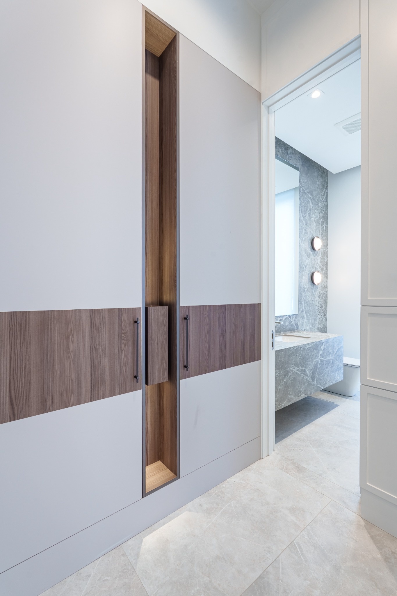 Custom wood cabinetry leading into a bright bathroom with stone finishes