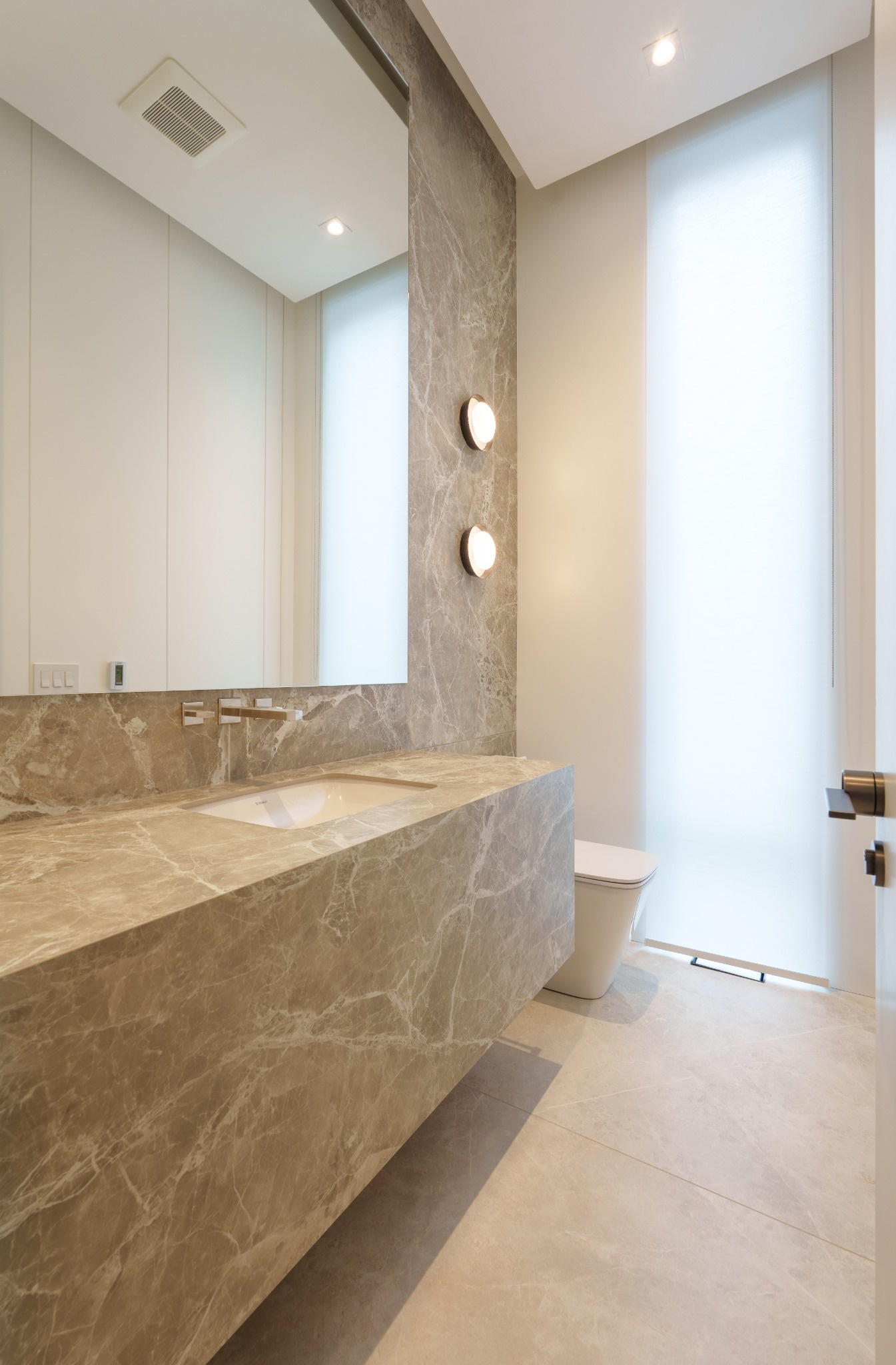 Modern bathroom vanity with natural stone countertop, large mirror, and wall lighting