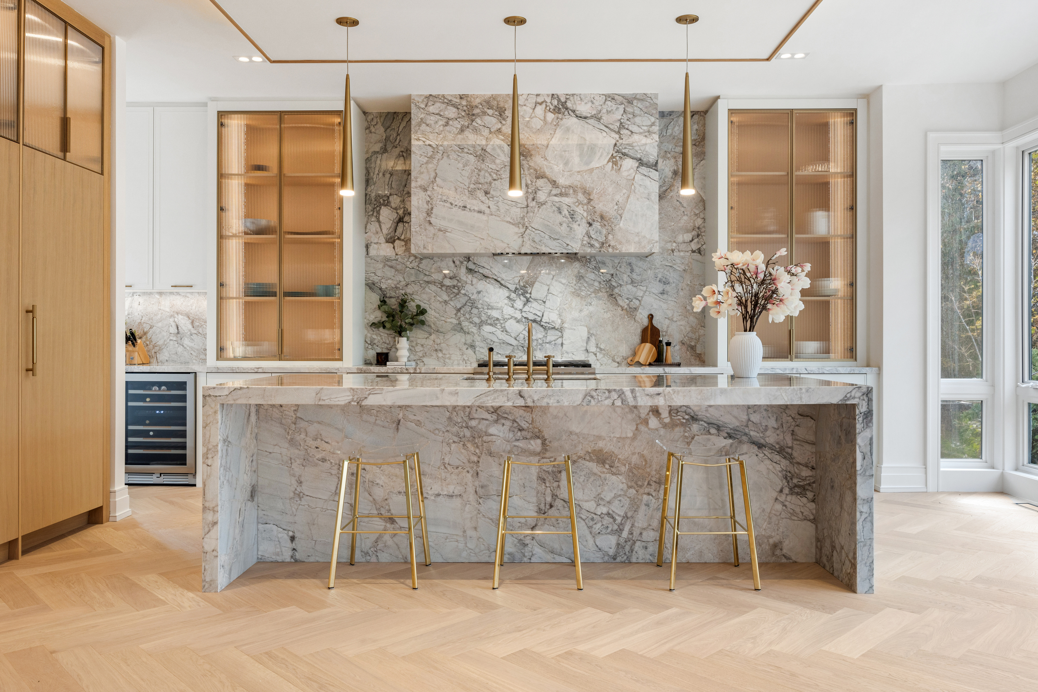 Luxury kitchen with dramatic stone island, matching backsplash, glass-front cabinetry, and gold stools