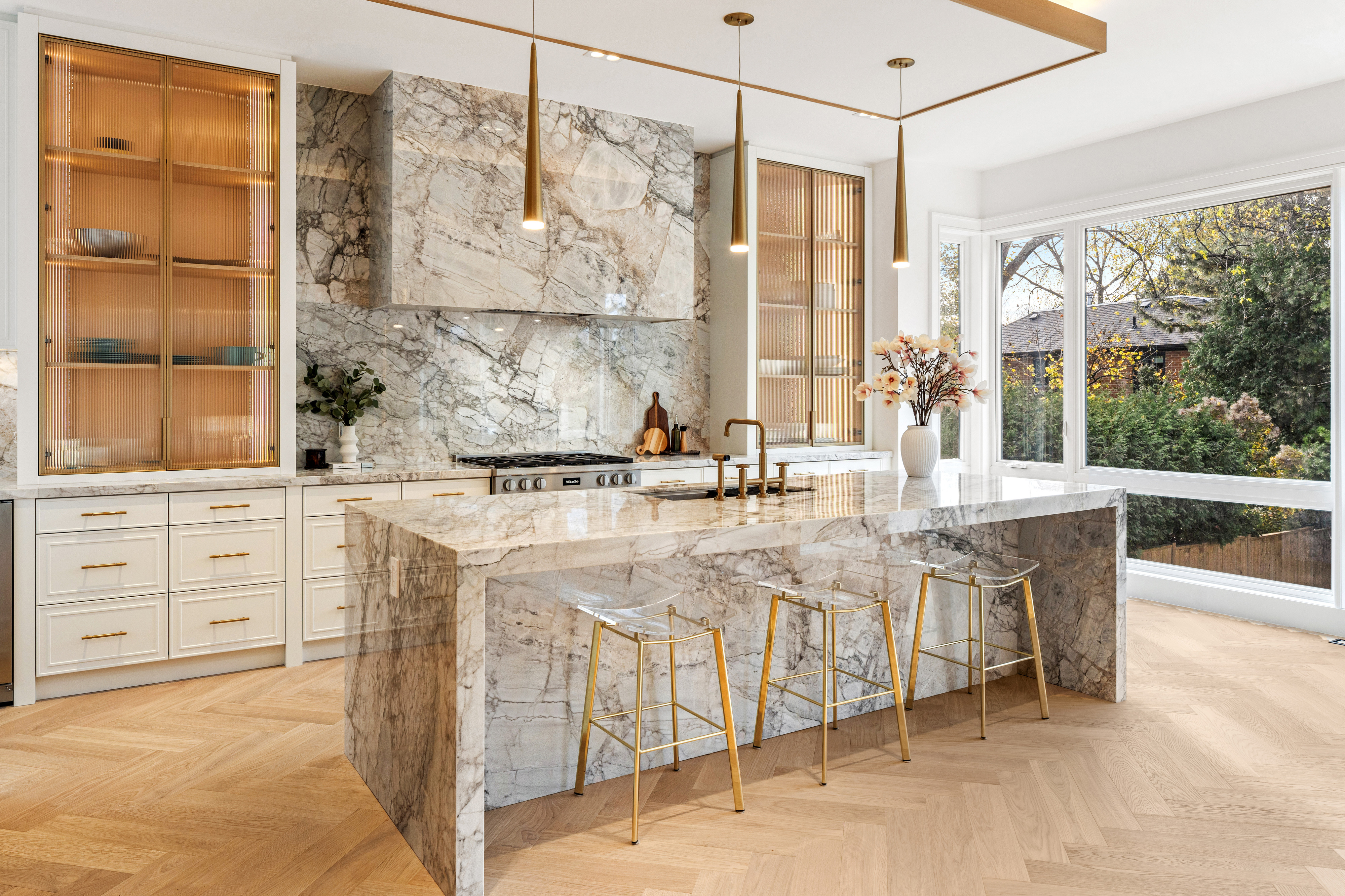 Bright kitchen with stone island, illuminated wood cabinetry, pendant lights, and garden views